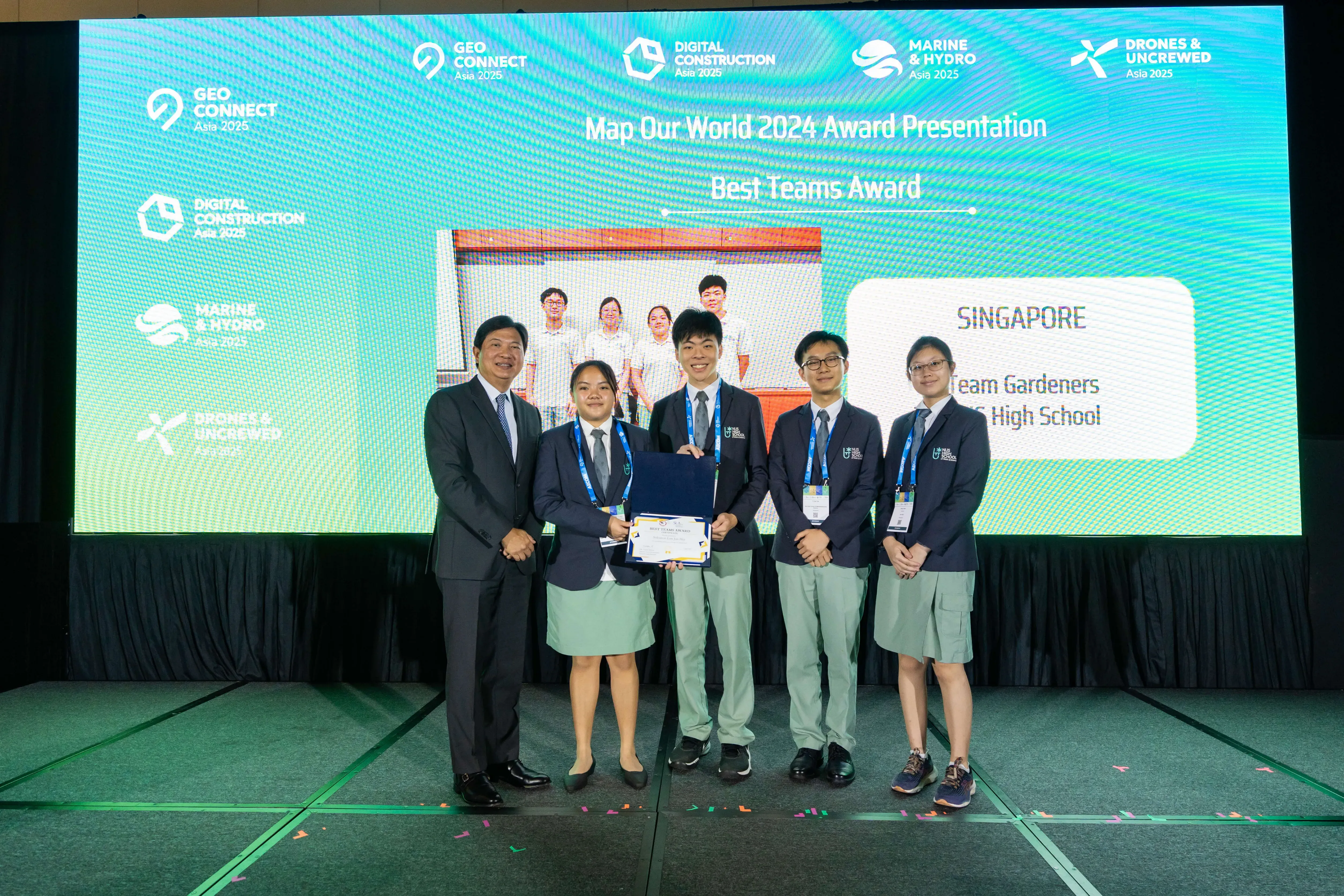 Group on stage holding a certificate at Best Teams Award presentation; screen behind reads SINGAPORE.